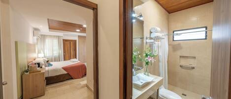 A hotel room with a bed, bedside table, and a bathroom with a shower, toilet, and sink.
