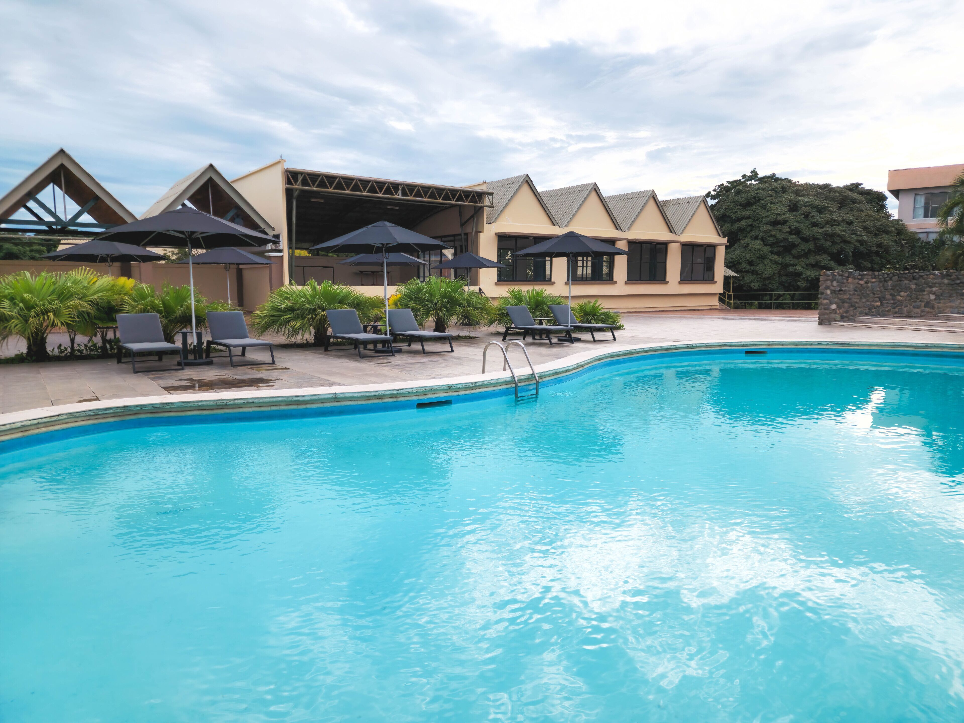A swimming pool with lounge chairs and umbrellas, surrounded by a building with a modern design.