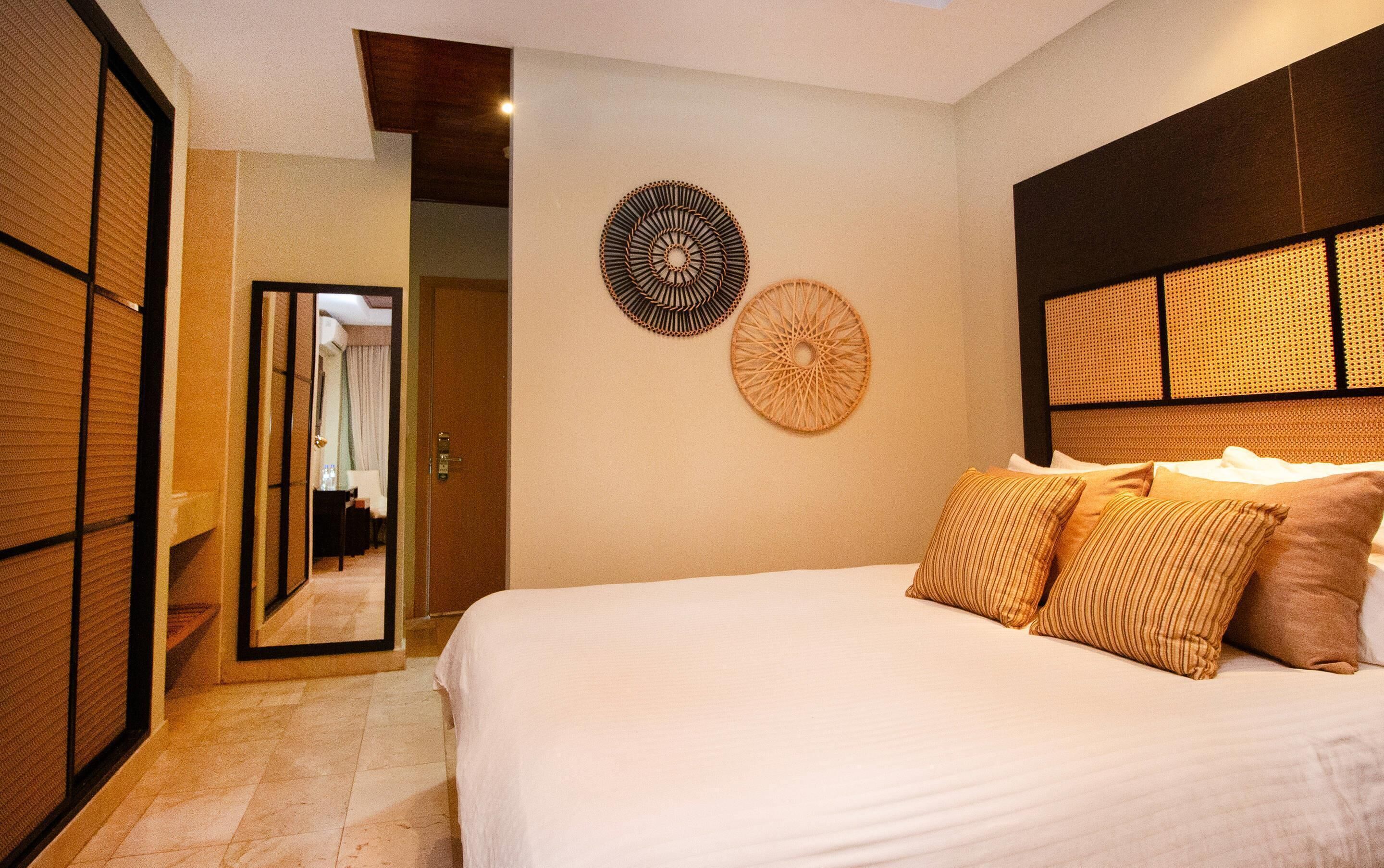 A bedroom with a bed, pillows, a mirror, and two wall decorations.