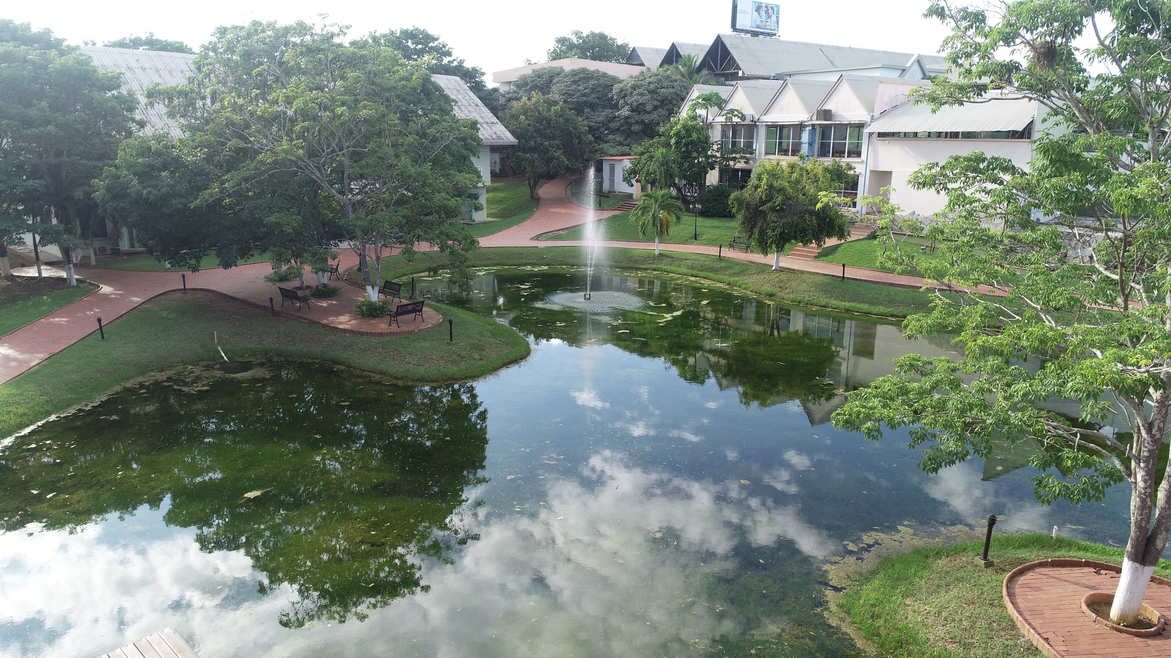 A serene pond with a fountain, surrounded by a well-maintained lawn and pathways.