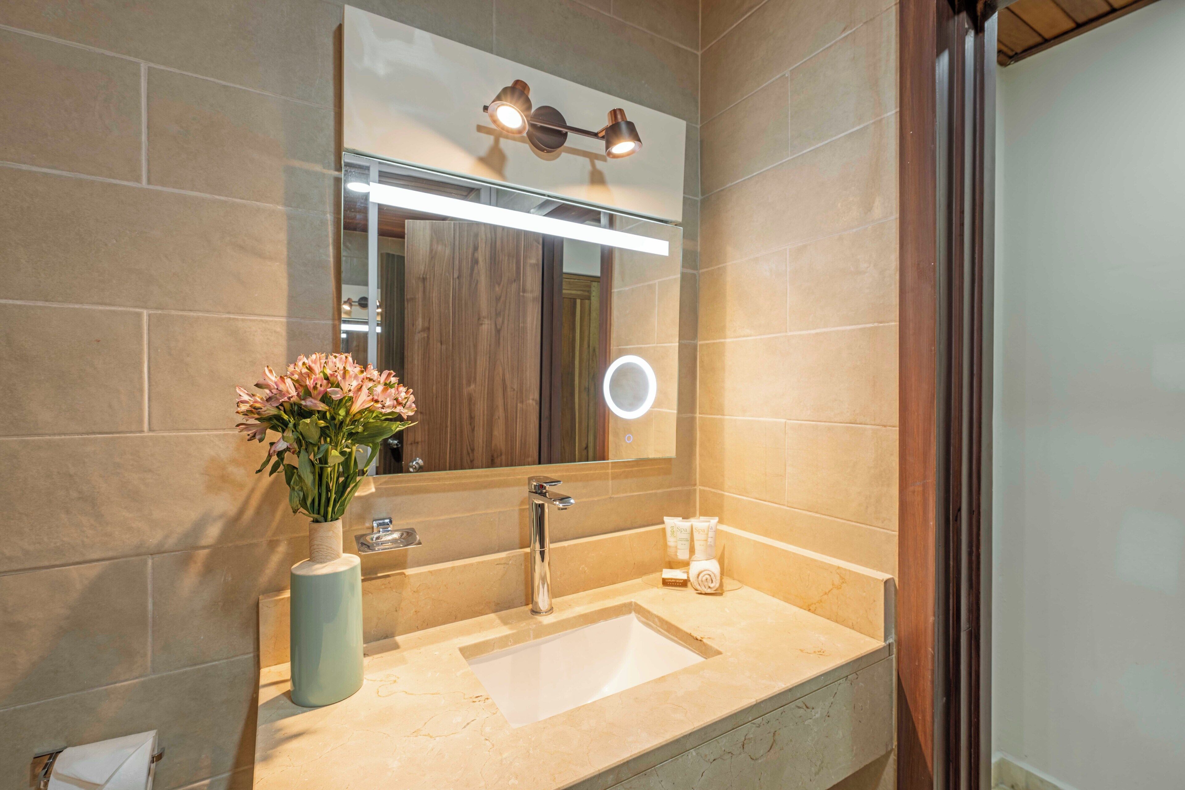 Une salle de bain avec un grand miroir, un lavabo et un vase de fleurs.