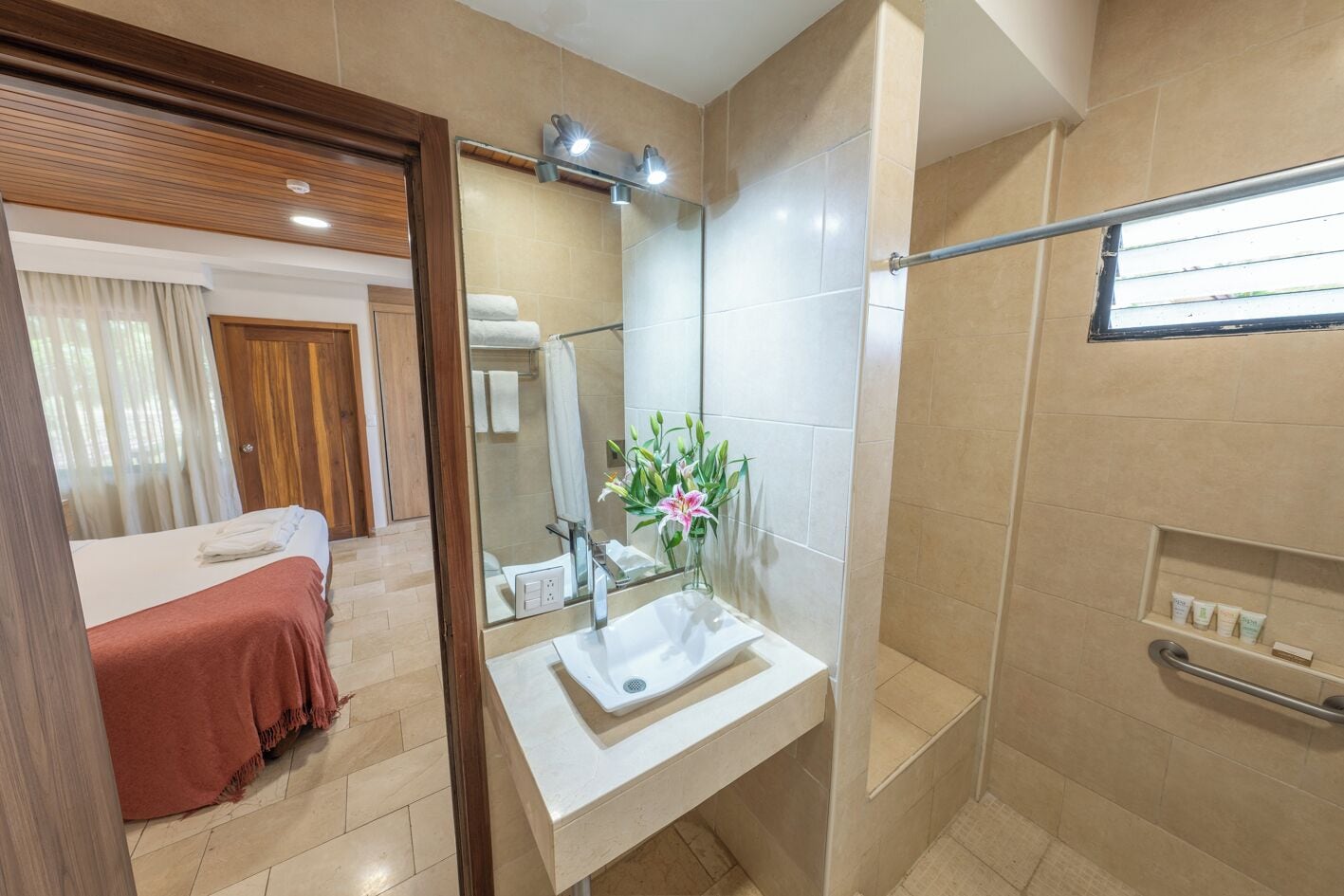 A hotel room with a bed, a bathroom with a sink and mirror, and a shower area.