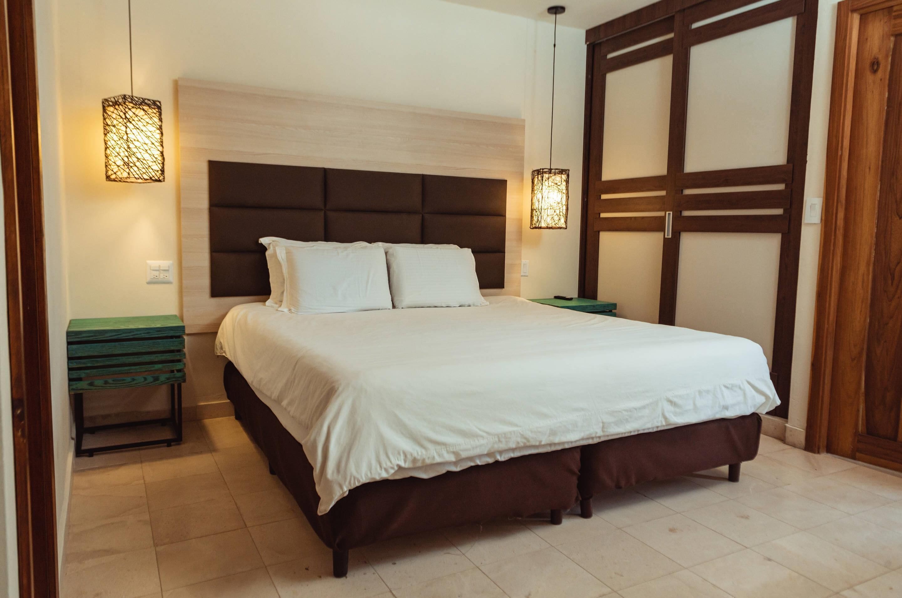 A bedroom with a large bed, two bedside tables, a wooden wardrobe, and two wall-mounted lamps.