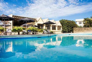 Piscina con sillas de descanso y sombrillas, un área de estar cubierta y un muro de piedra.