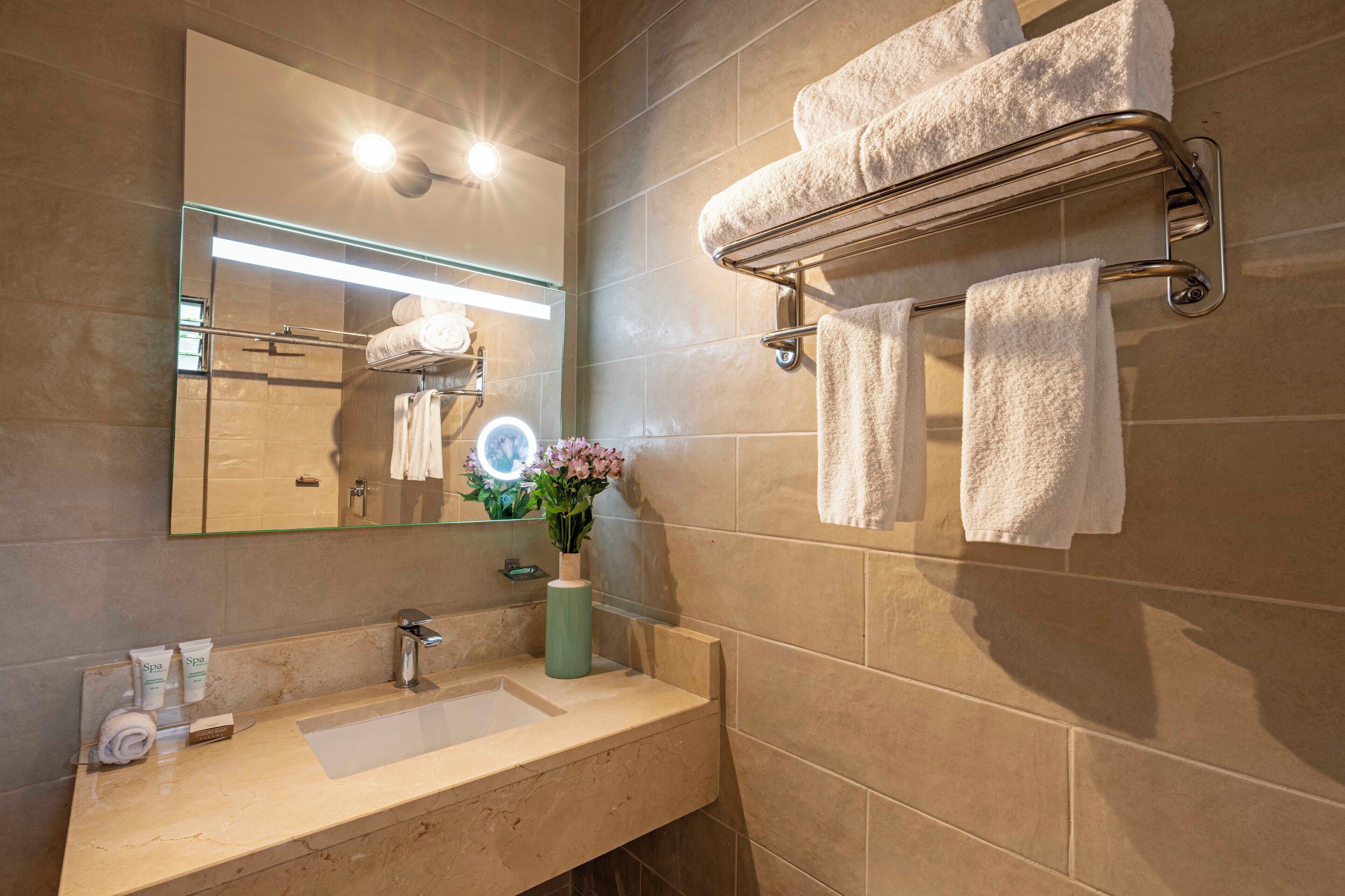 Un baño con lavamanos, espejo, toallero y un florero con flores.