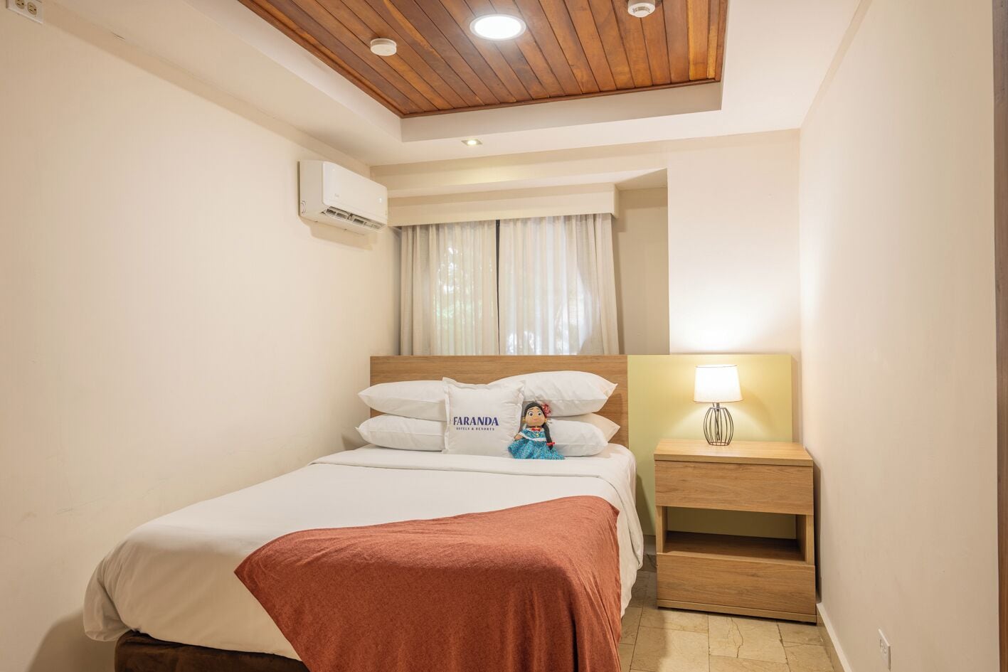 Habitación de hotel con cama, mesita de noche con lámpara, ventilador de techo y ventana con cortinas.
