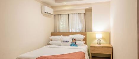 Habitación de hotel con cama, mesita de noche con lámpara, ventilador de techo y ventana con cortinas.