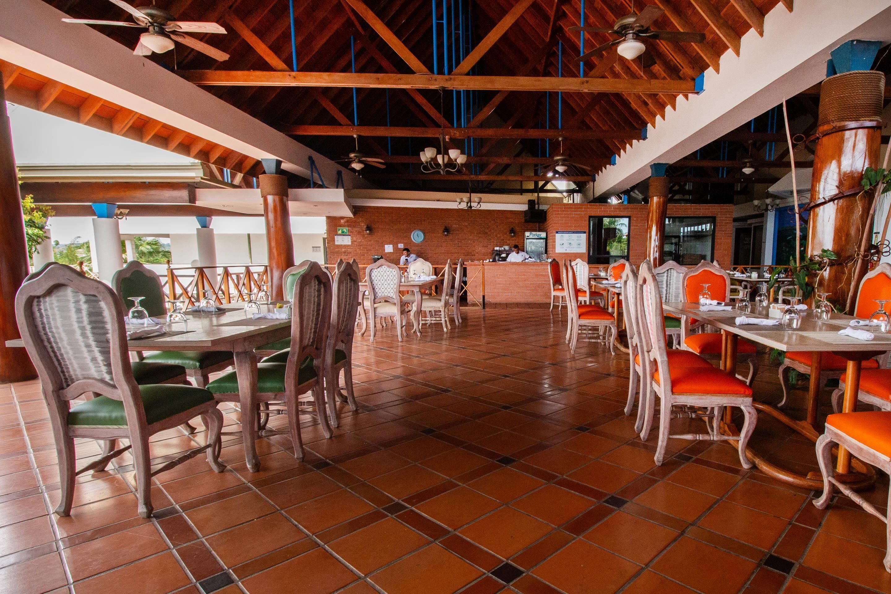 Un restaurant avec des poutres en bois, un sol carrelé et des chaises rembourrées de tissu vert.