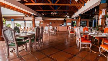 Un restaurante con vigas de madera, suelo de baldosas y sillas verdes con cojines.