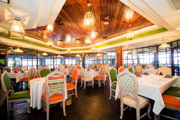 A restaurant with multiple tables and chairs, large windows, and a wooden ceiling.