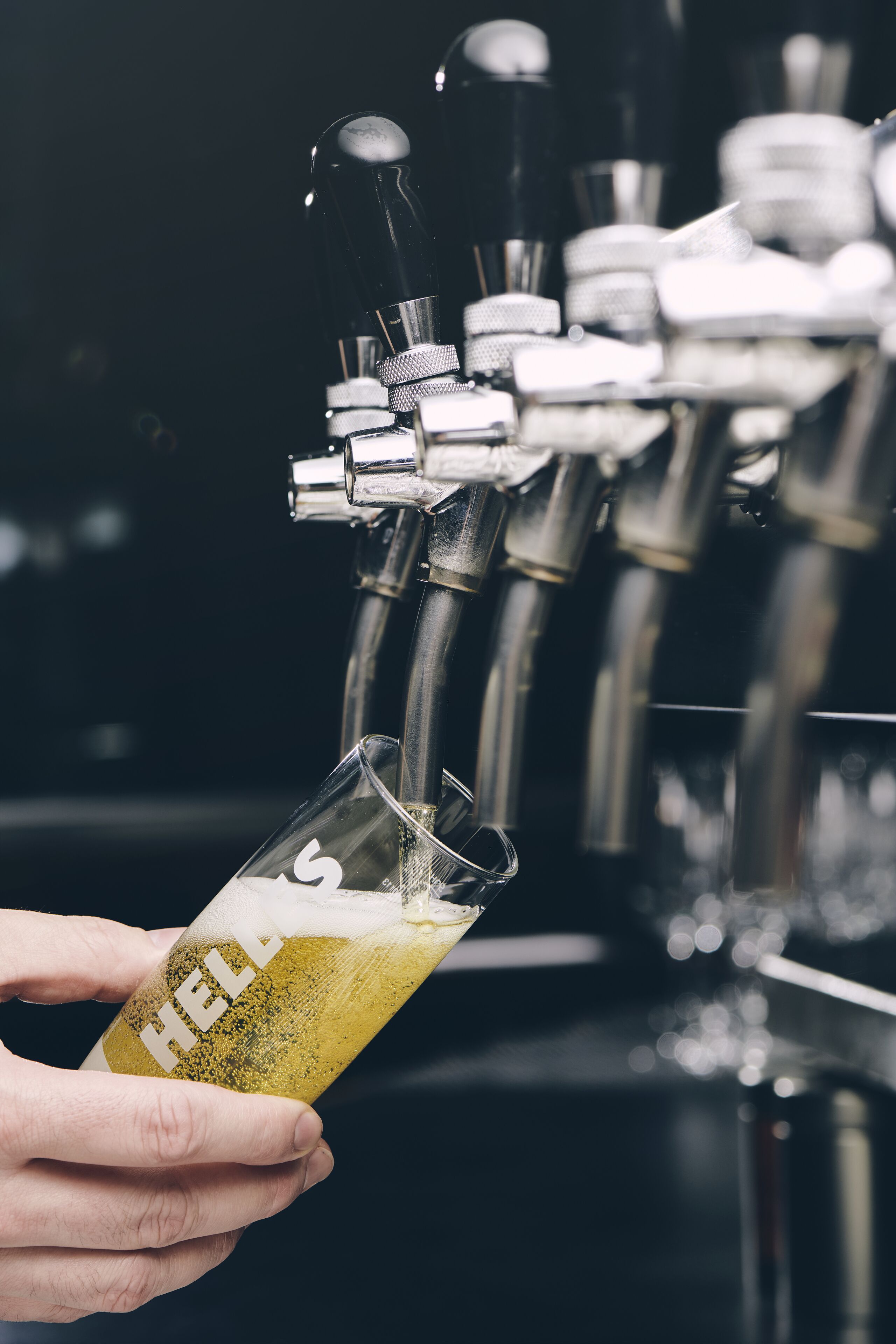 A hand holding a glass with a label reading "HELL" as beer is poured from a tap.