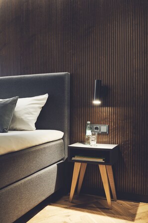 A modern bedroom with a dark grey sofa, a bedside table with a lamp, and a wooden floor.