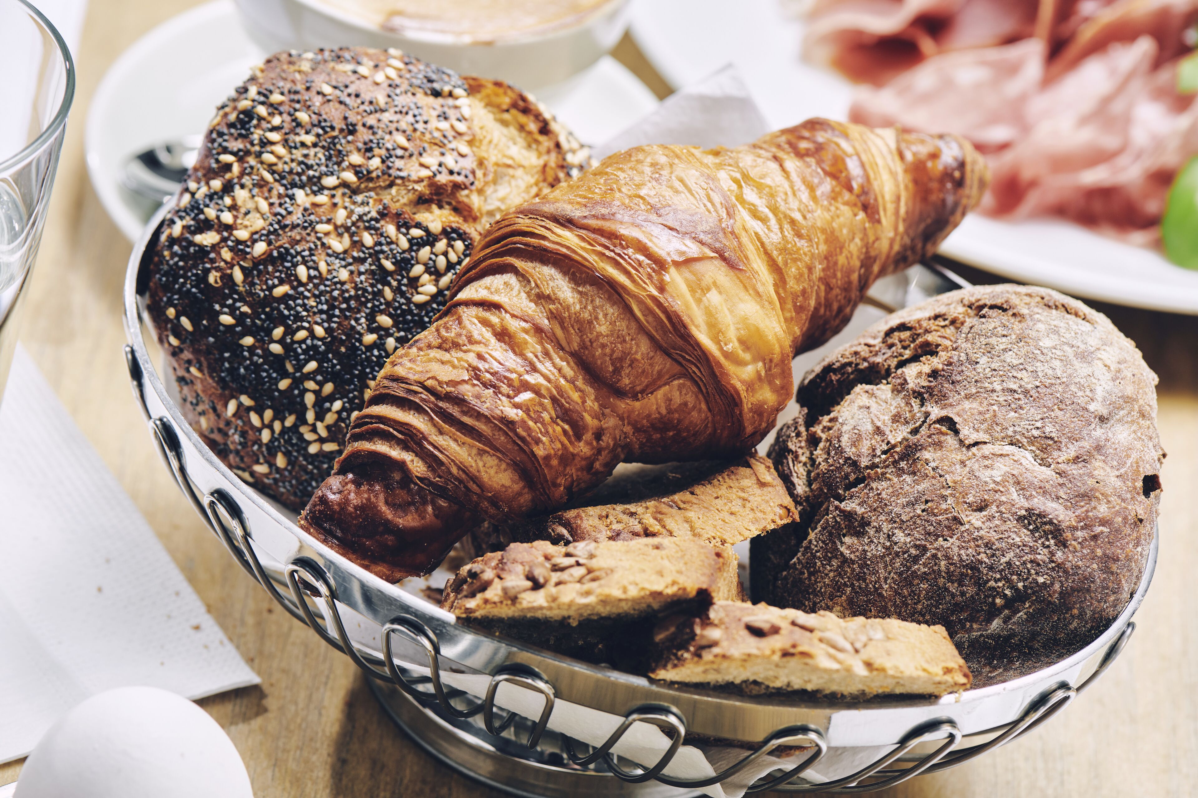 Un panier contenant divers produits de boulangerie, notamment un croissant, une miche de pain et un biscuit aux pépites de chocolat.