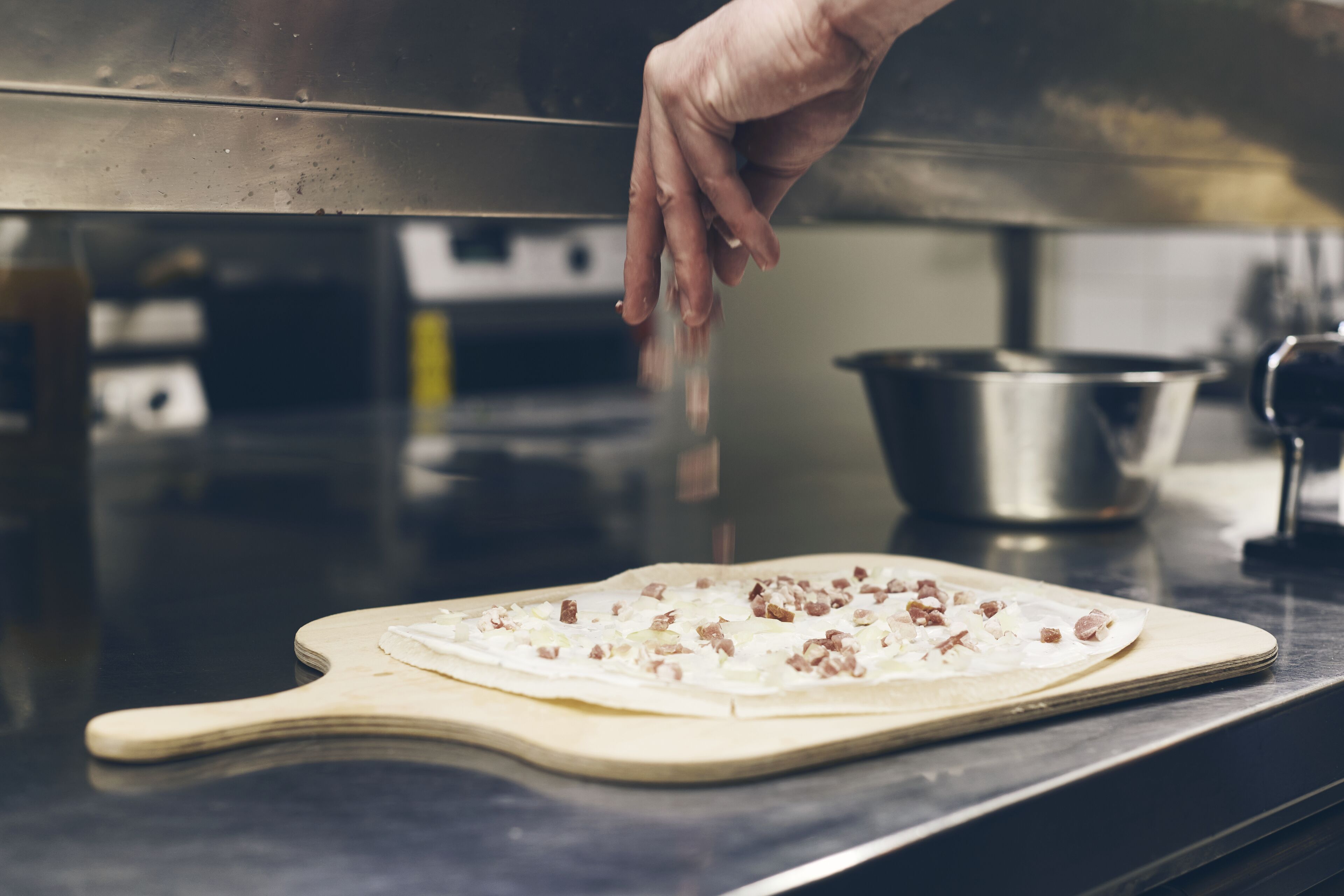 A hand placing a pizza on a wooden board in a kitchen.