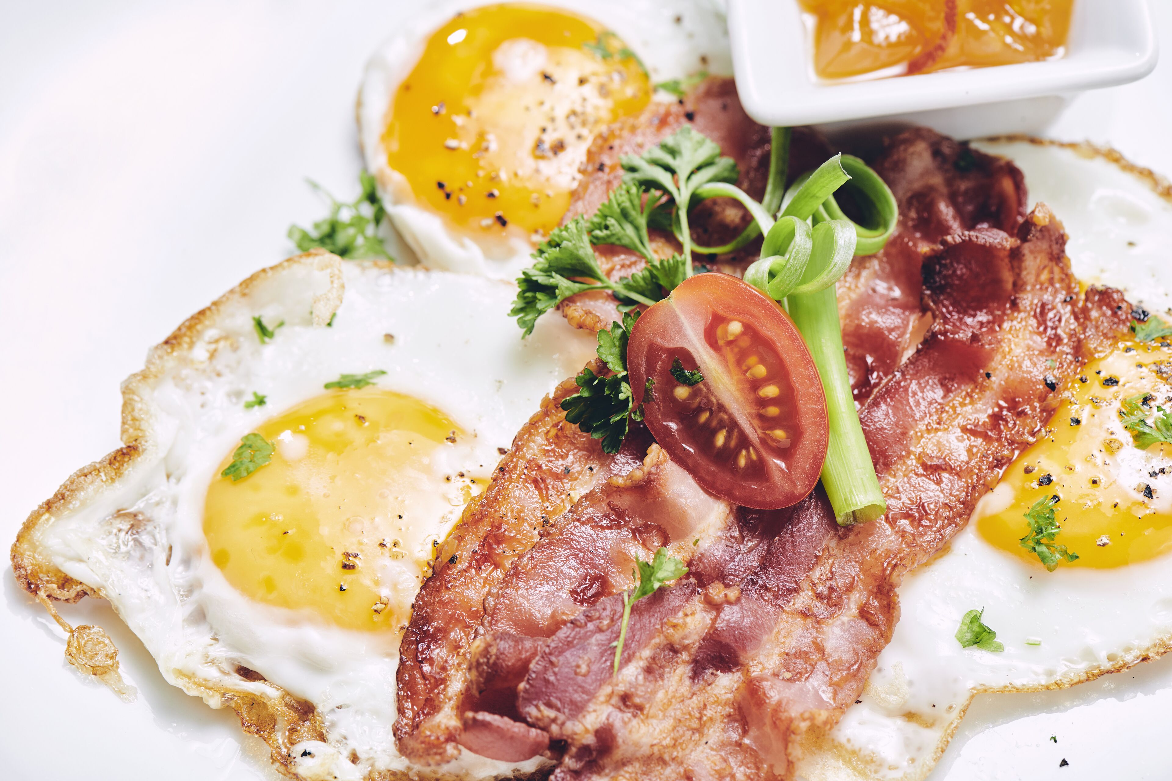 A breakfast plate with eggs, bacon, tomato, and greens.