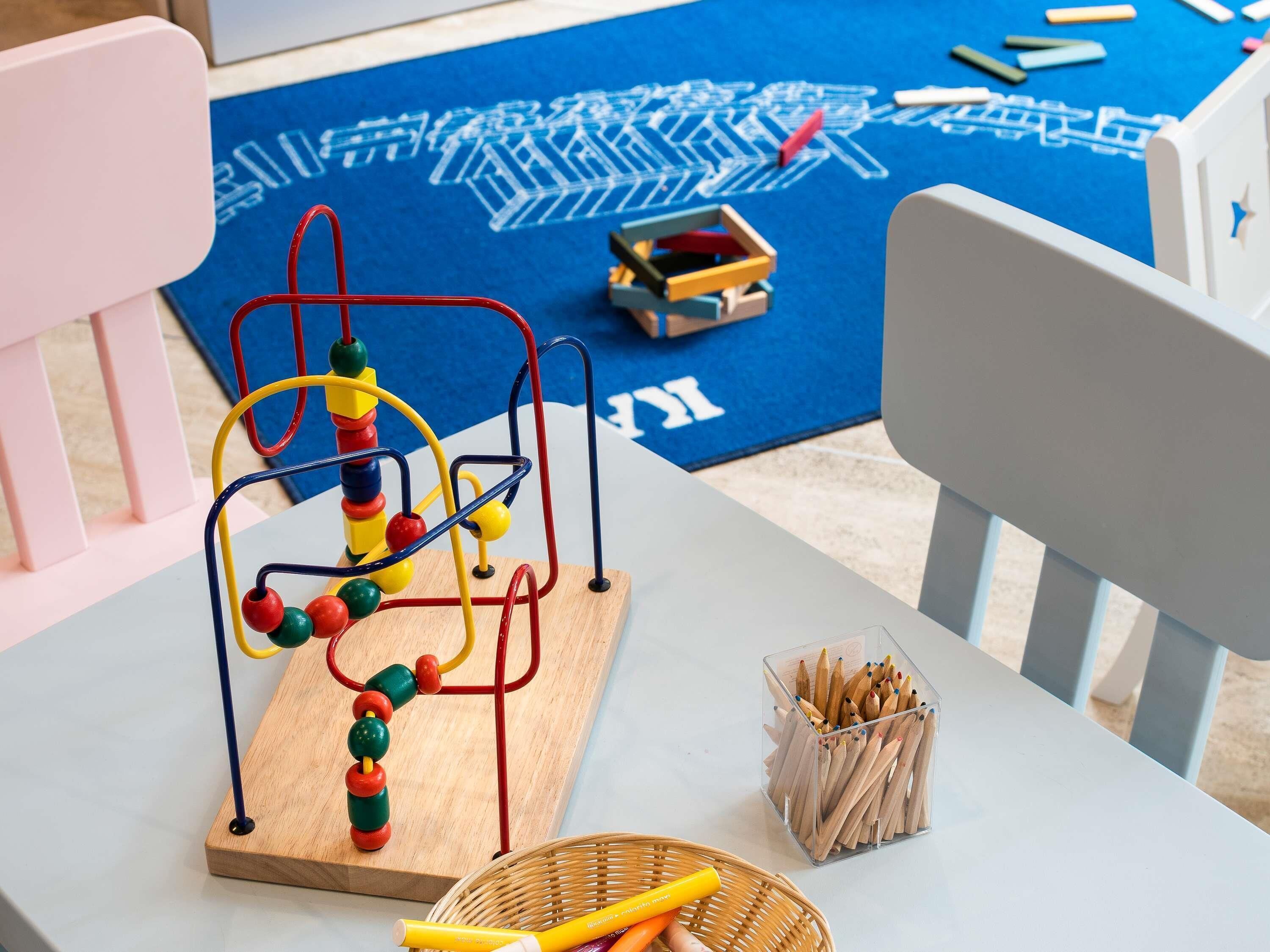 Ein Spielbereich für Kinder mit einer Holzkugellabyrinth, einem Tablett voller Buntstifte und einer blauen Matte mit weißen Mustern.