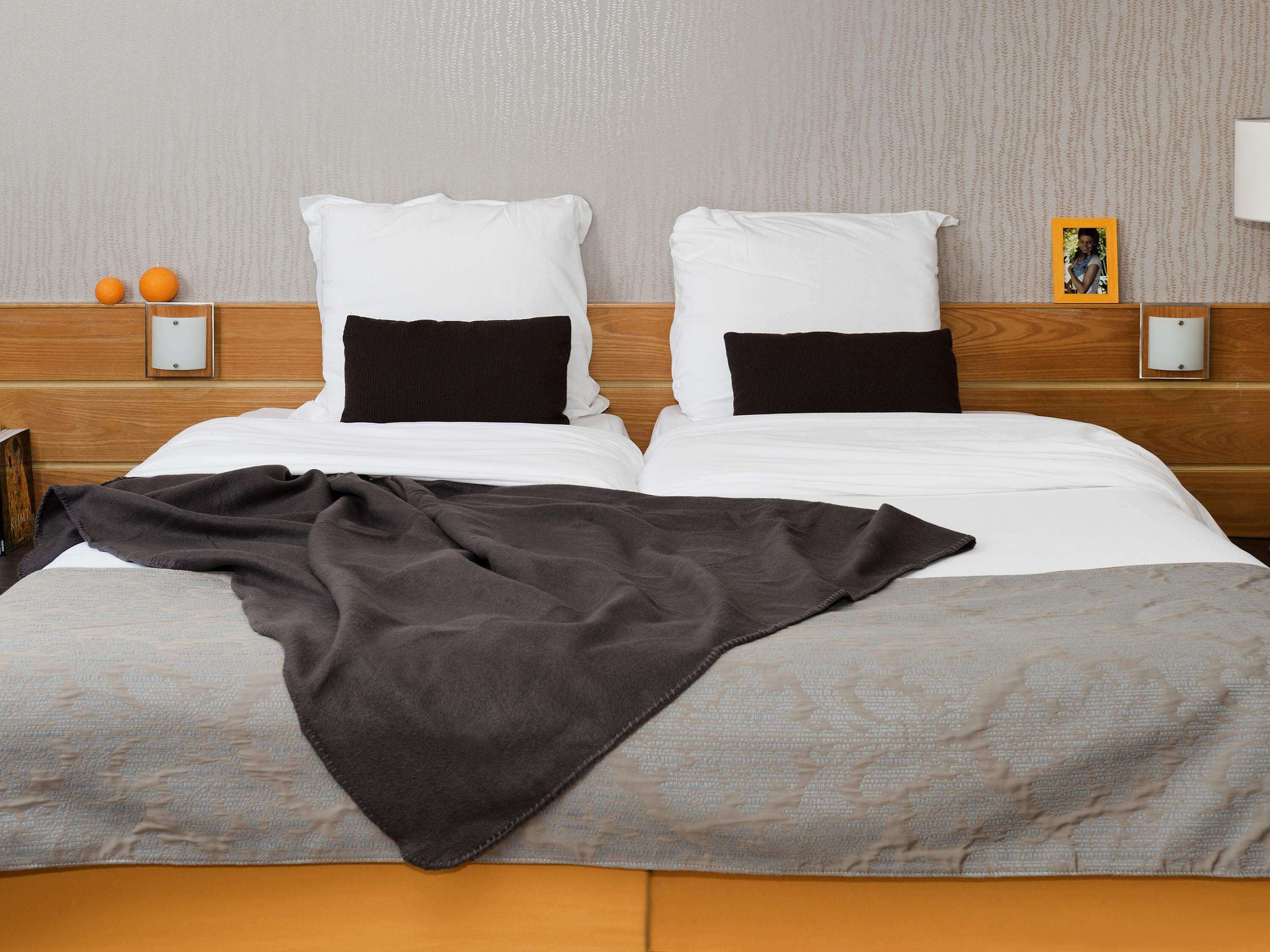 A neatly made bed with white and black pillows, a grey blanket, and a picture frame on the nightstand.
