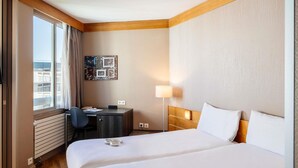 A hotel room with a large bed, a desk, a chair, a lamp, and a window with curtains. - Aparthotel Adagio Paris XV (Paris)