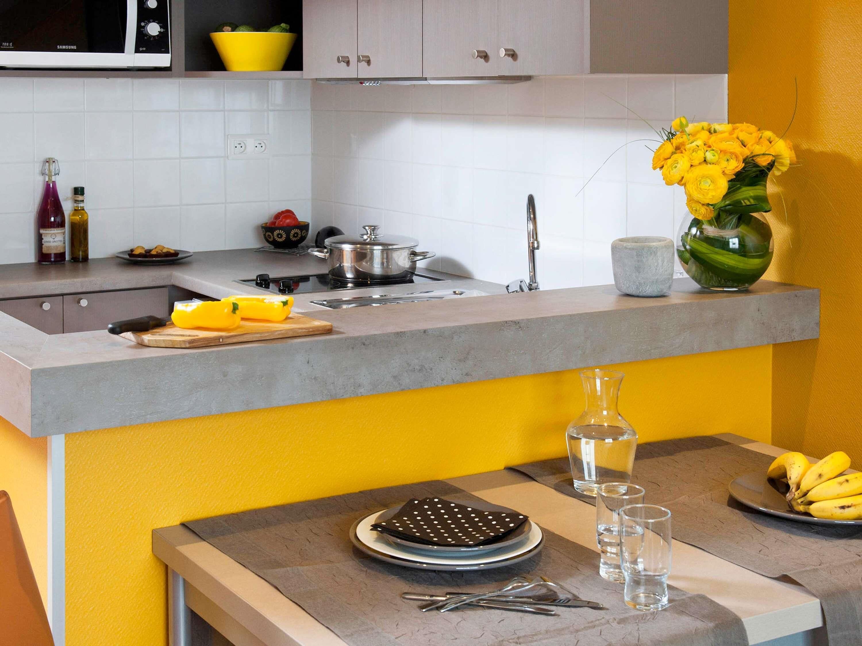 Une cuisine avec un plan de travail gris, un four à micro-ondes, un évier et un vase rempli de fleurs jaunes.