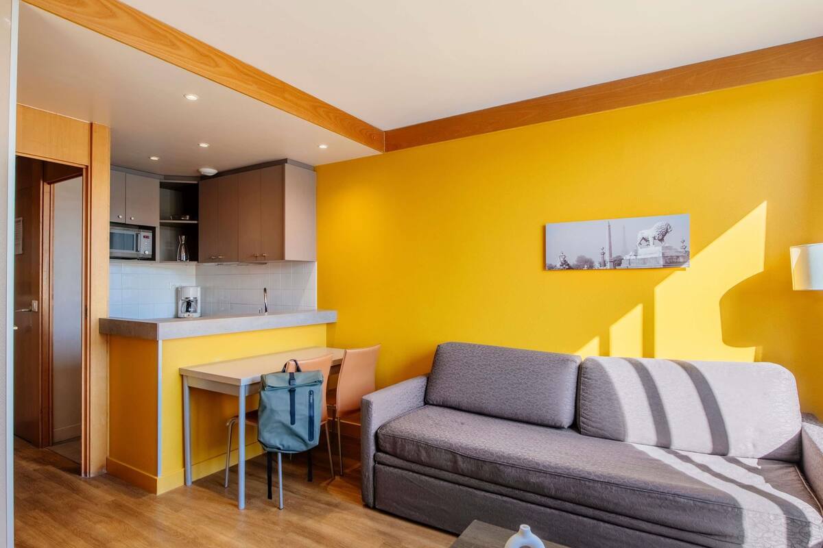 Un espacio habitable compacto con kitchenette, un sofá, una mesa de comedor y una silla.