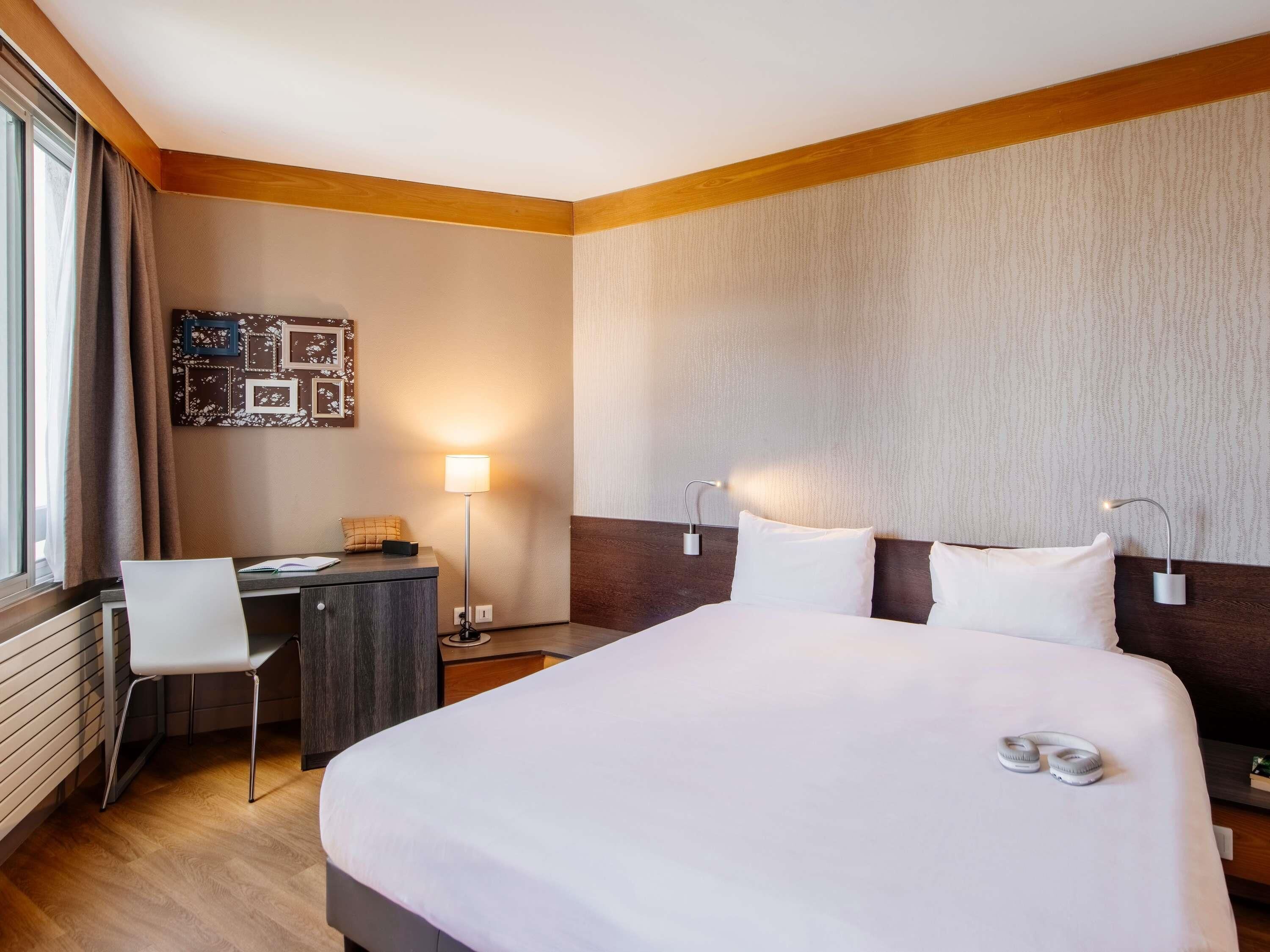 Une chambre d’hôtel équipée d’un lit, d’un bureau, d’une chaise et d’une lampe fixée au mur.