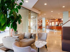A modern lobby with a sofa, chairs, a marble table, and a reception desk.