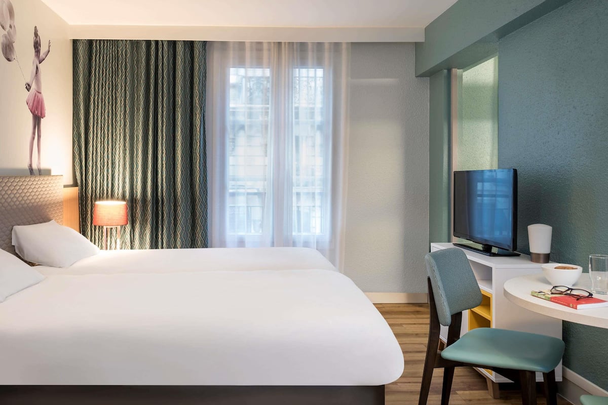 Een hotelkamer met een bed, een bureau met een televisie, een stoel en een lamp.