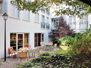 A courtyard with a table and chairs, a lamp post, and a building with large windows and shutters. - Aparthotel Adagio Paris Montmartre (Paris)
