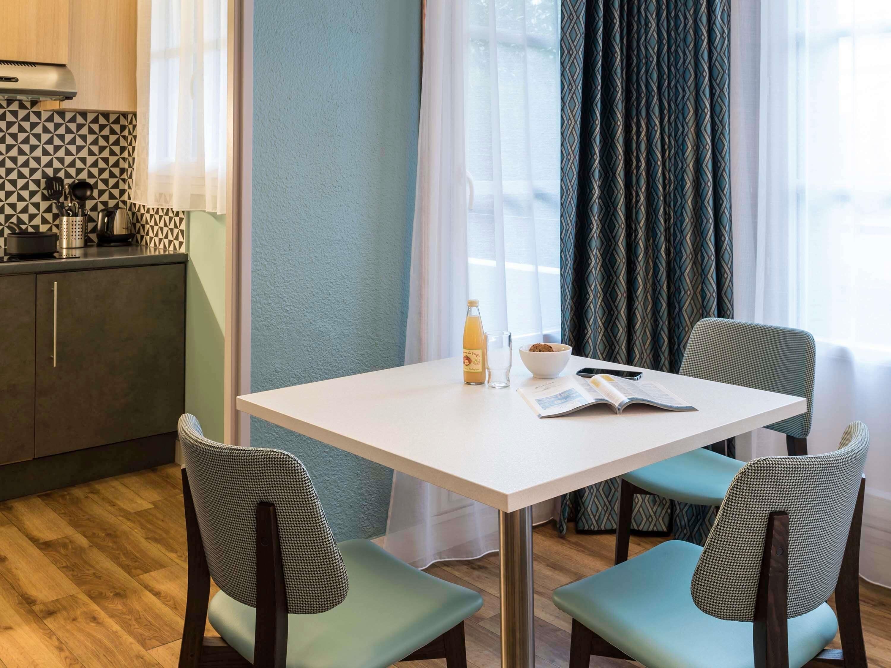 A small dining area with a white table, two chairs, a bowl of cereal, a bottle of orange juice, and a book.