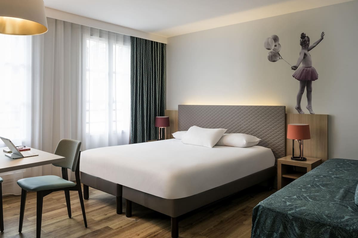 Een hotelkamer met een bed, een bureau, een stoel, een lamp en een kunstwerk aan de muur.