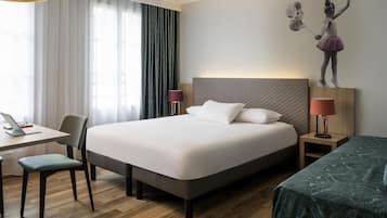 A hotel room with a bed, a desk, a chair, a lamp, and a wall-mounted artwork.