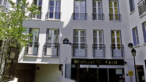 Um edifício de vários andares com varandas, uma placa com a inscrição "Residence Montmartre" e um céu azul claro.