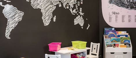 A room with a world map on the wall, a small table with storage bins, and a bookshelf with books.