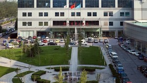 A modern building with a glass facade, multiple flags, and a parking lot. - Beijing Jinjiang Fuyuan Hotel (Beijing)