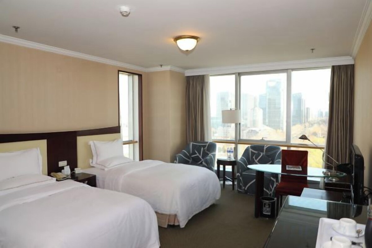 Une chambre d’hôtel avec deux lits, un bureau avec une chaise, une télévision et une vue sur la ville.