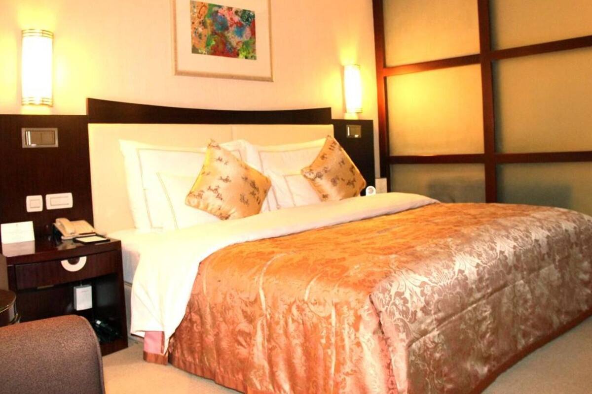 Una habitación de hotel con una cama grande, una mesita de noche con teléfono, un escritorio con lámpara y un cuadro en la pared.