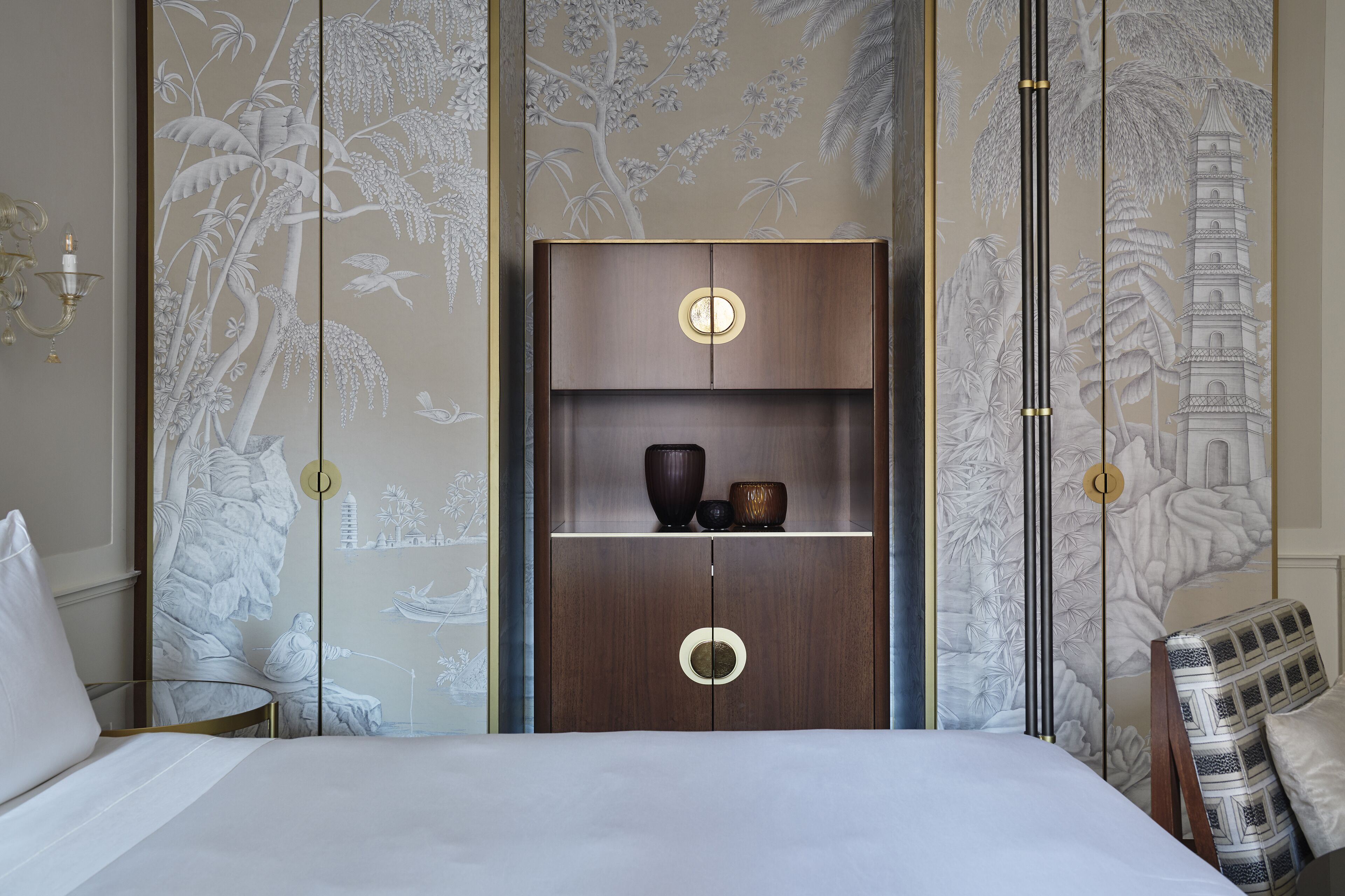 Une chambre d’hôtel avec un lit, une armoire en bois dotée de deux tiroirs et un mur orné d’une fresque.