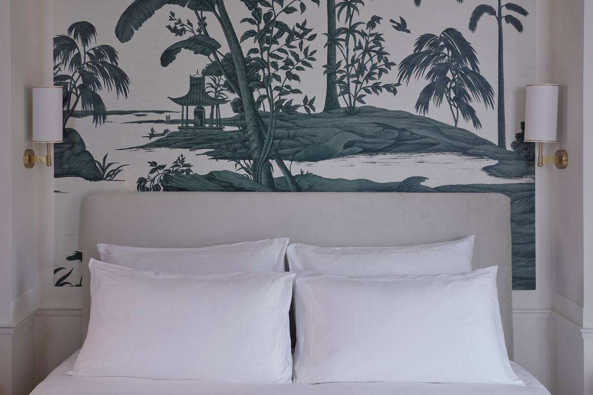 A bed with white bedding and a headboard, flanked by two wall-mounted lamps with gold accents.