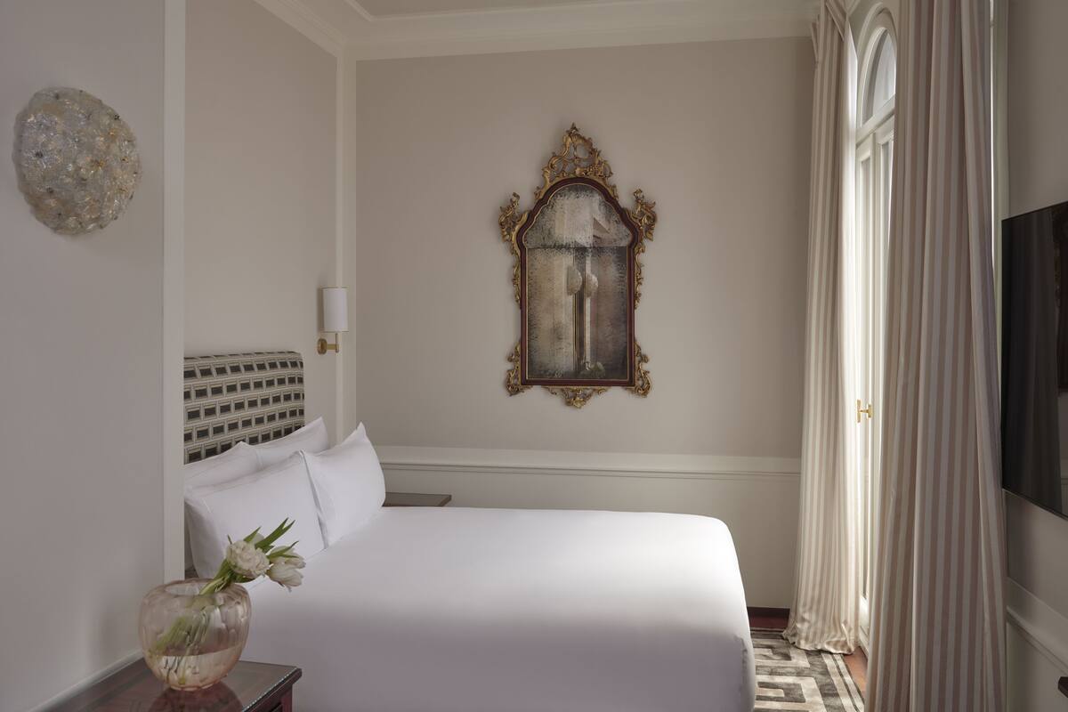 A hotel room with a large bed, a decorative mirror, a vase with flowers, and a television.