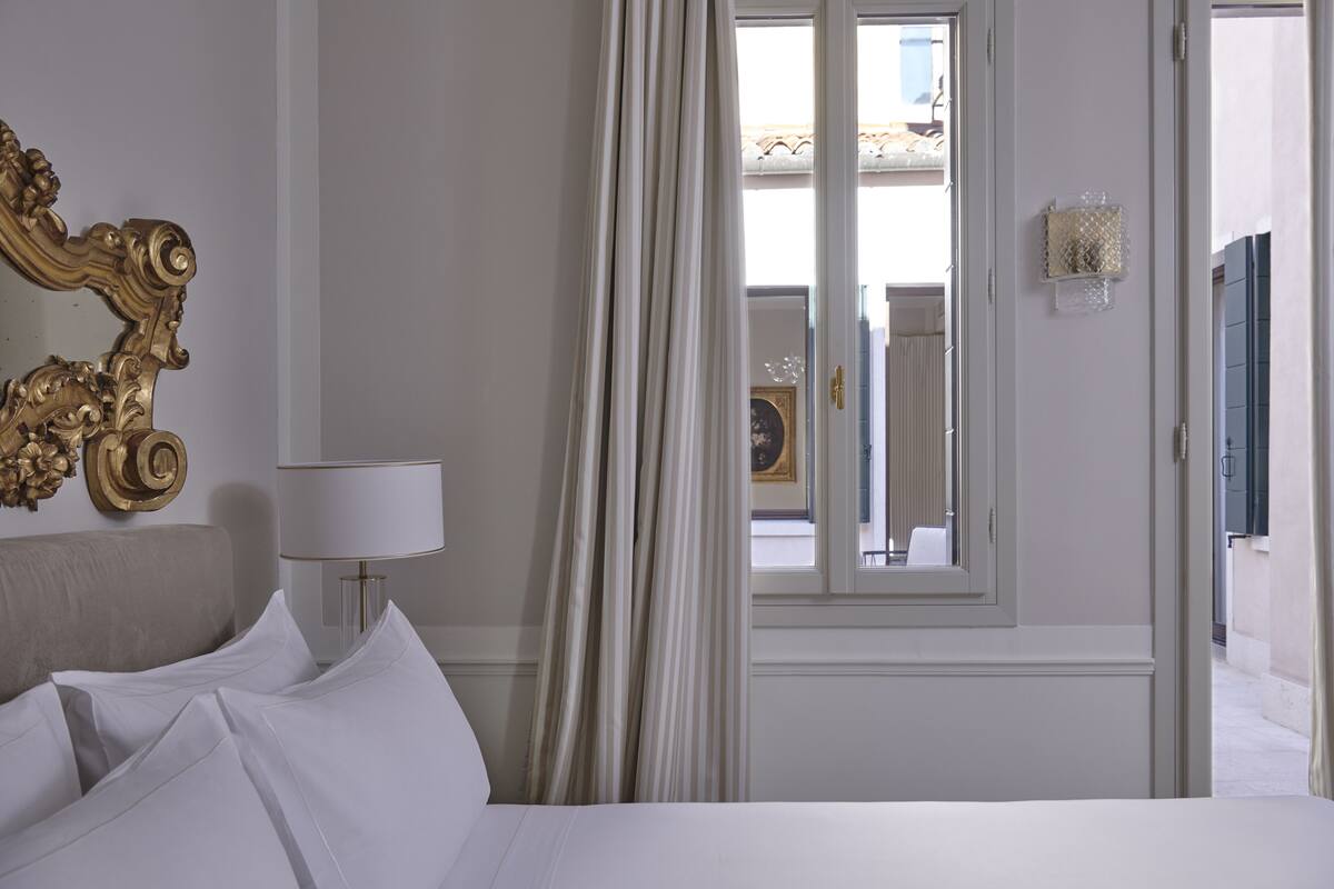 A hotel room with a bed, a lamp, a window with curtains, and a view of the outside.
