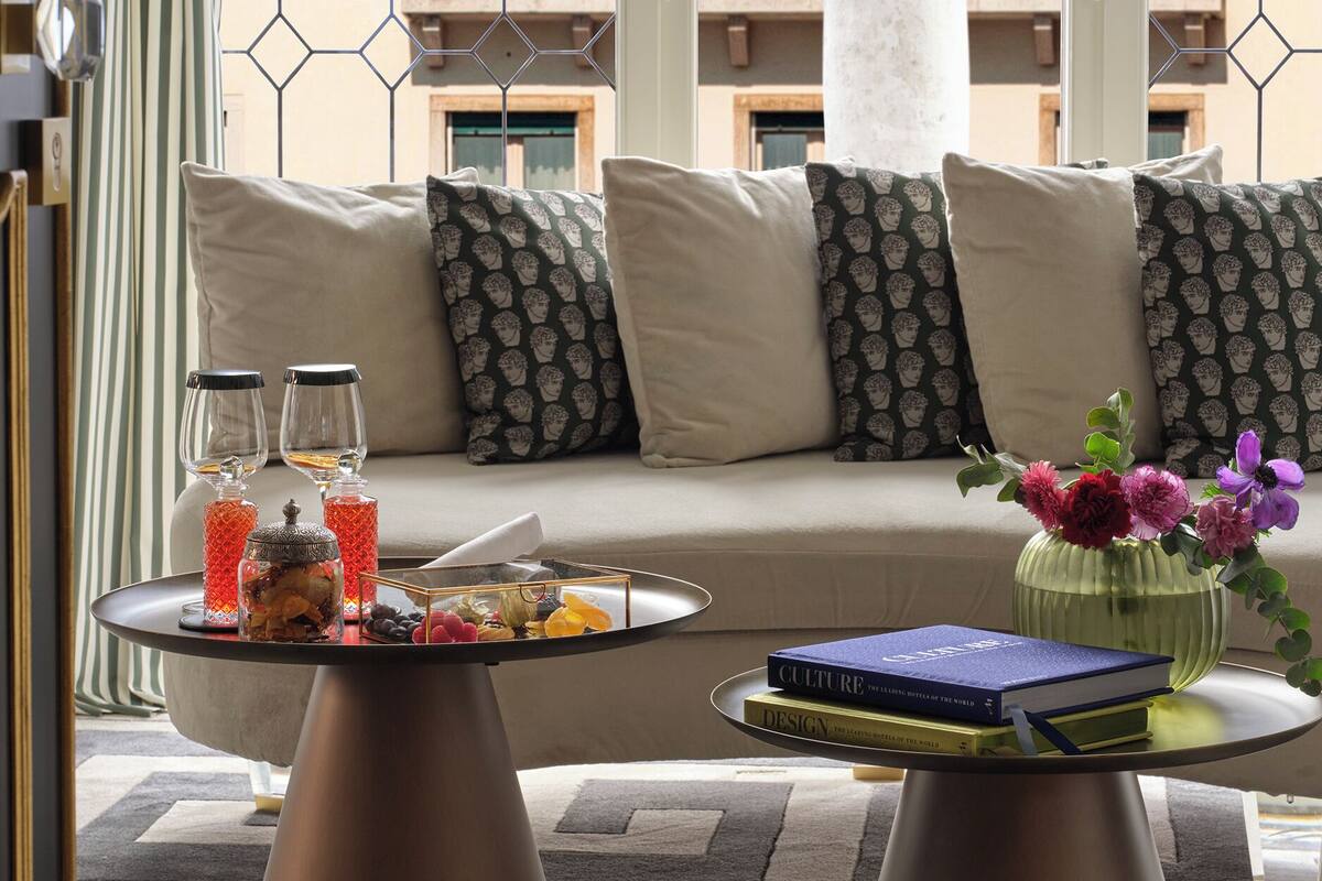 A modern living room with a sofa, two coffee tables, a decorative vase, and a view of a building through a geometric window.