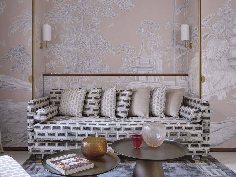 Een kamer met een gestreept bankje, een ronde tafel en een decoratieve wand met een natuurmotief.