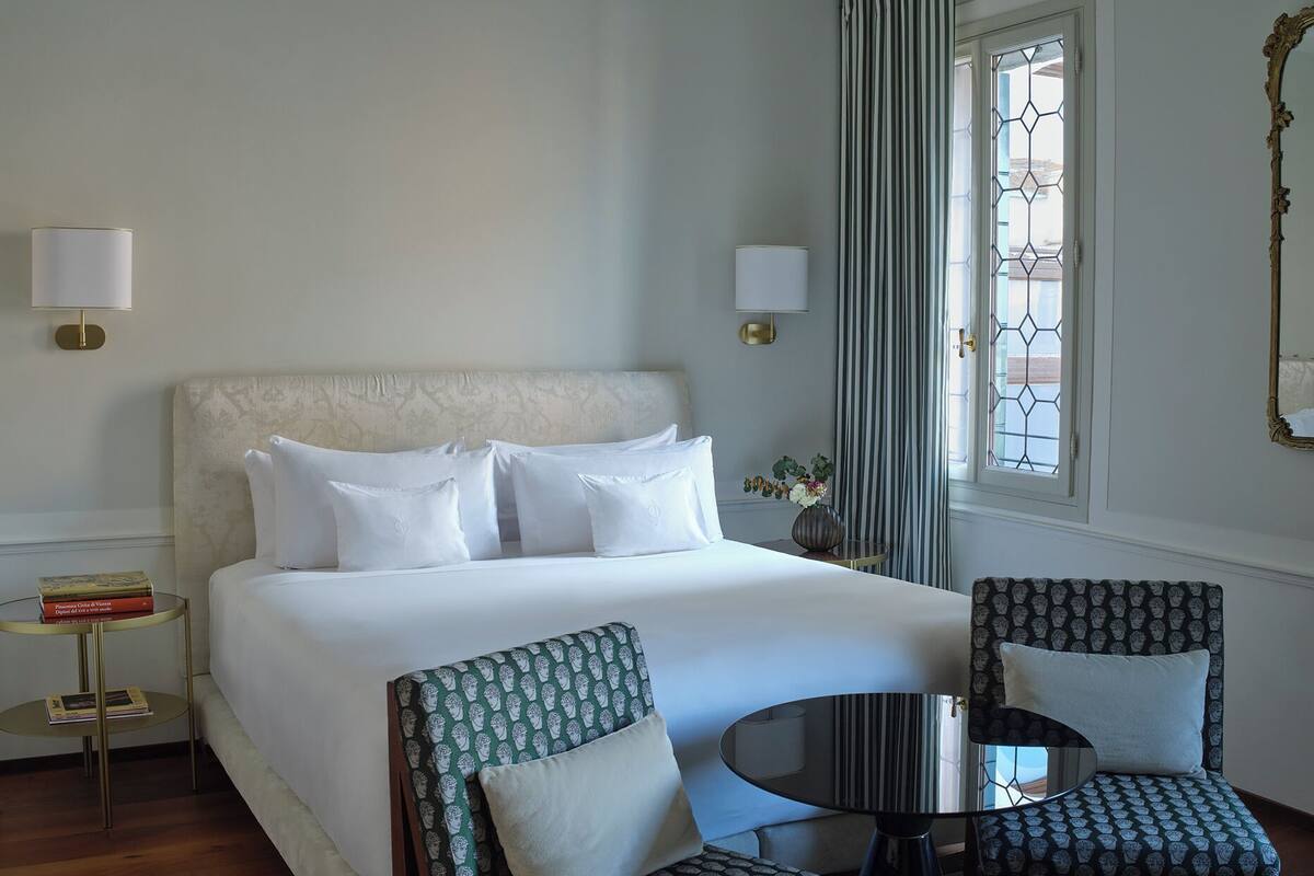 A hotel room with a large bed, two armchairs, a small round table, and a window with curtains.
