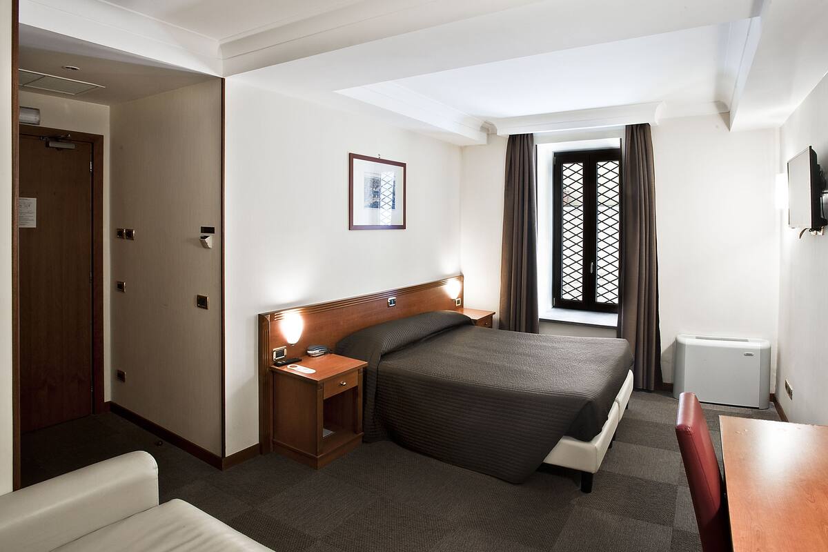 Une chambre d’hôtel avec un lit, une table de chevet et une fenêtre avec des rideaux.