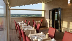 Ein Restaurant mit gedeckten Tischen, Blick auf die Landschaft und einer Tür an der Seite.