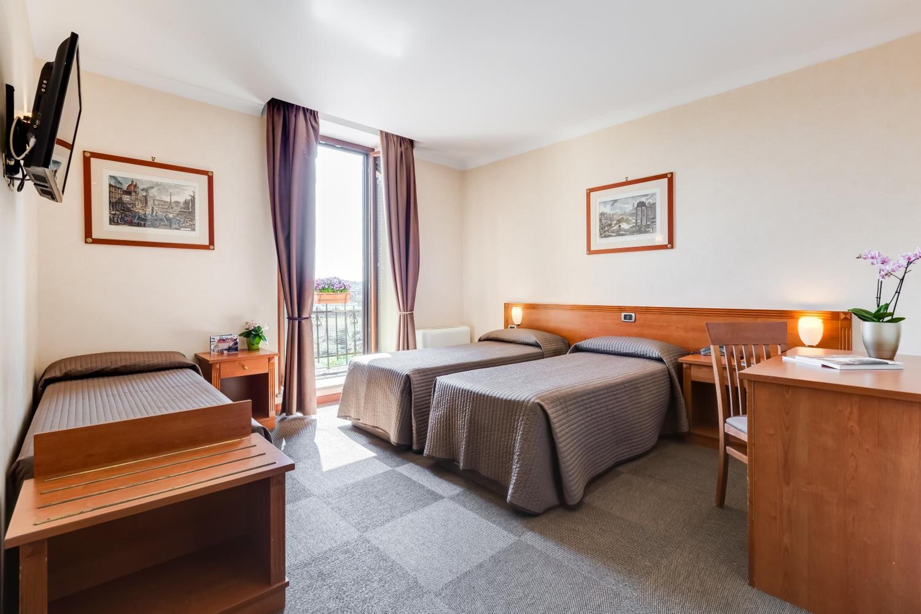 Habitación de hotel con dos camas, un escritorio, una silla, una mesita y un ventanal con cortinas.