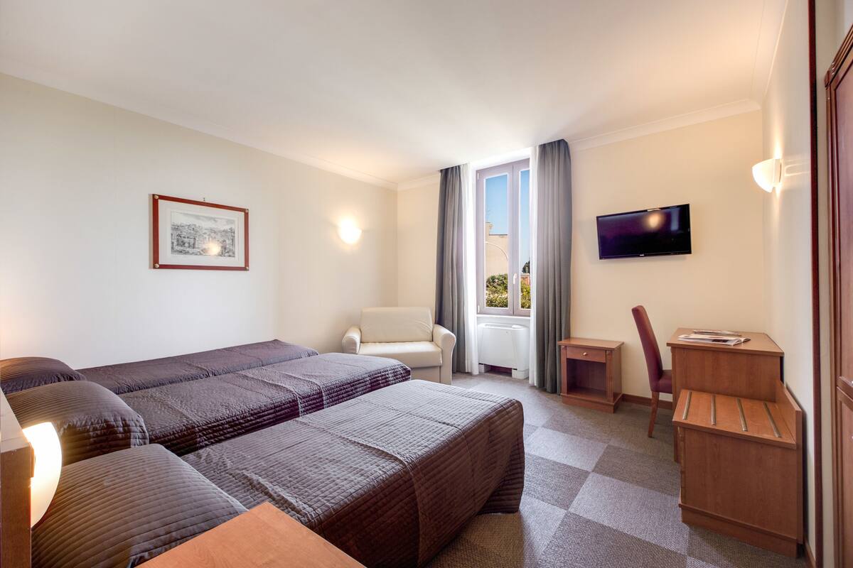 Une chambre d’hôtel avec deux lits, un bureau, une chaise, une télévision et une fenêtre avec des rideaux.
