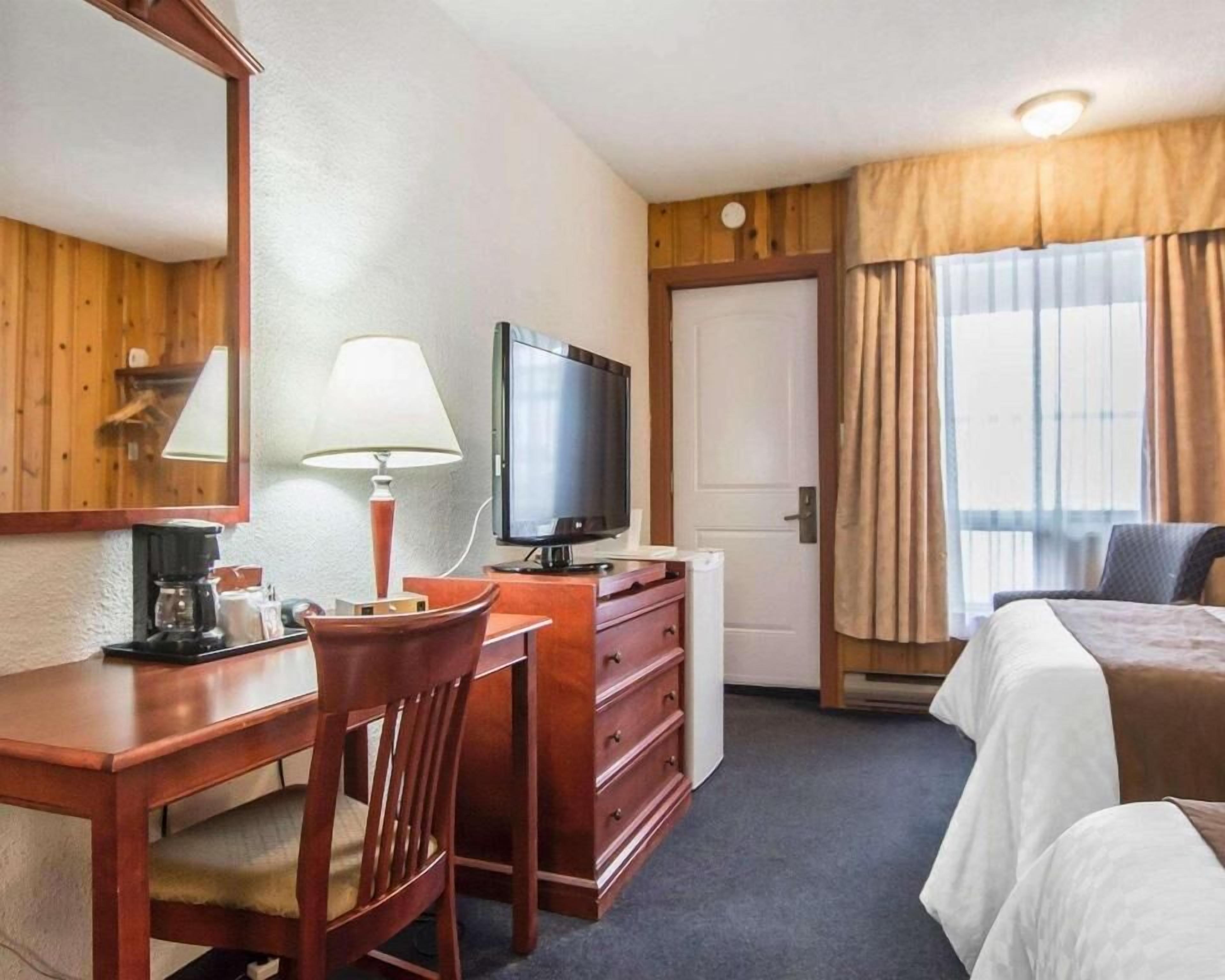 A hotel room with a desk, chair, television, and a bed.