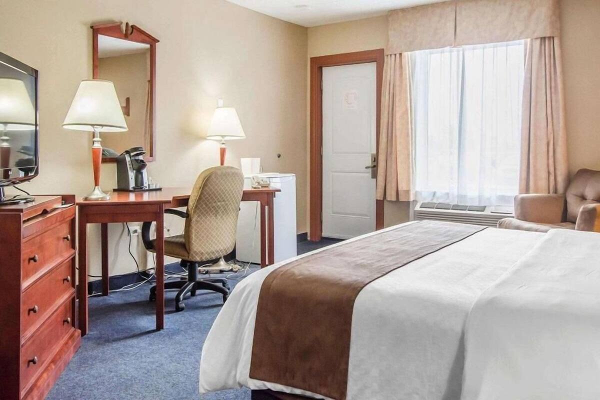 A hotel room with a bed, desk, chair, dresser, and a large window with curtains.