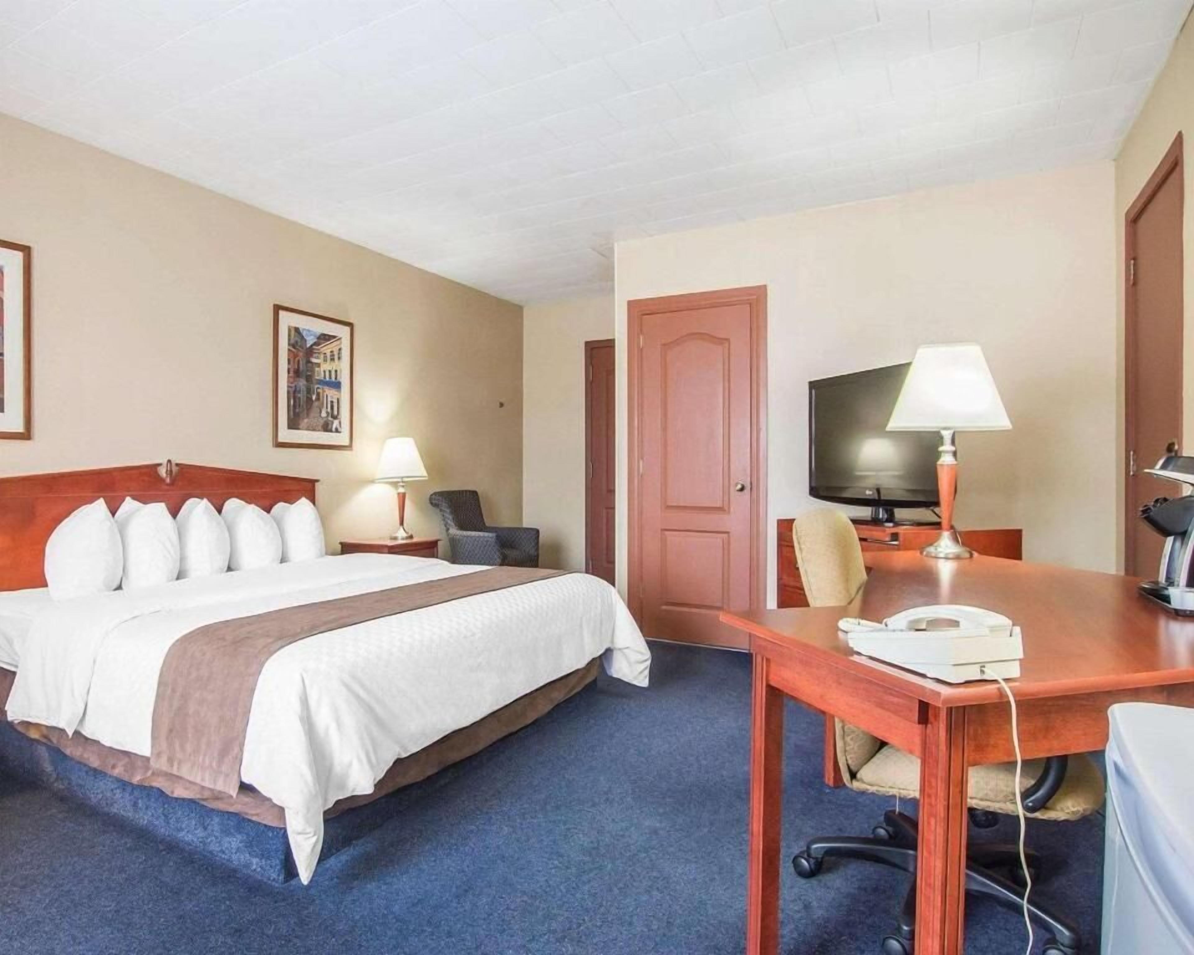 A hotel room with a bed, two bedside tables with lamps, a TV, a desk with a telephone, and a door.